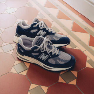 A pair of New Balance Made in UK sneakers in front of a rabbit in a brown textured studio environment. 