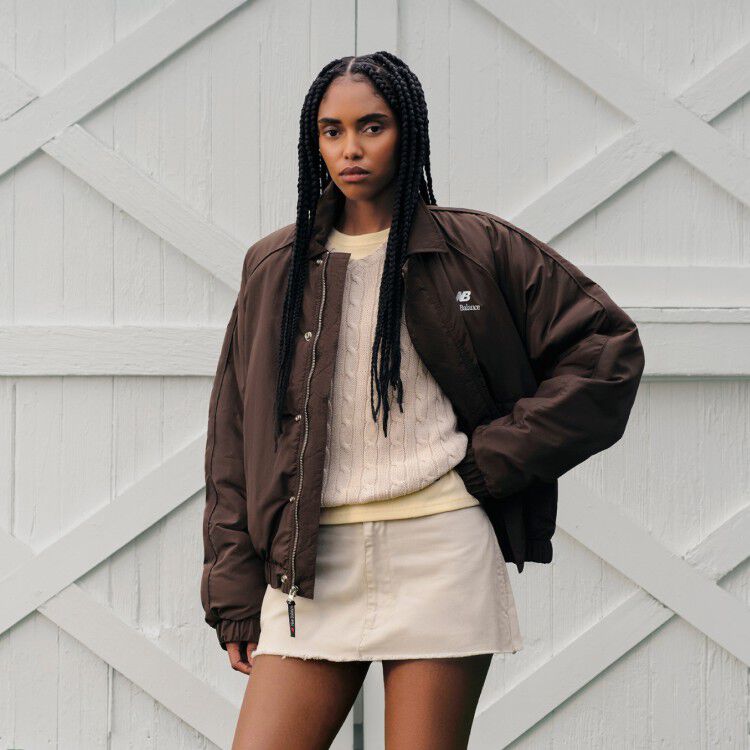 A woman standing in front of a barn wearing a New Balance jacket.