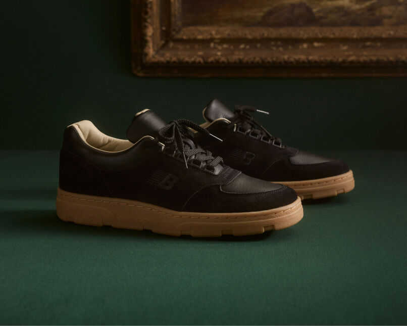 Knee down view of a man wearing a pair of New Balance Made in UK sneakers standing on a patterned tile floor.  