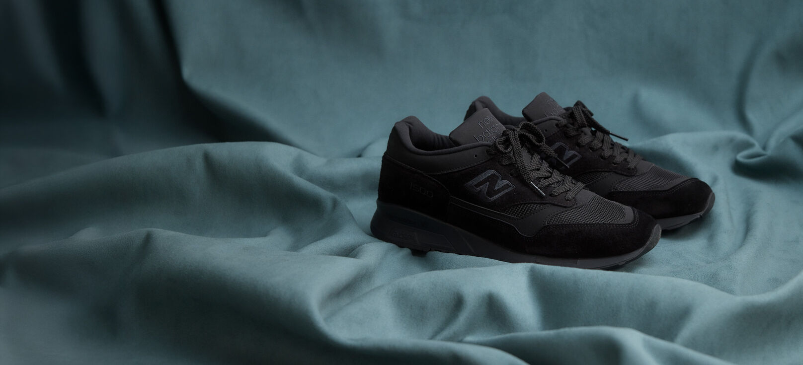A pair of New Balance Made in UK sneakers on a flowing blue sheet backdrop.  