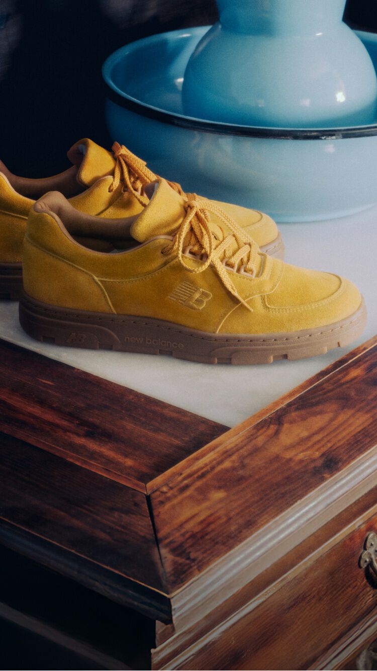 A pair of New Balance Made in UK sneakers on an antique wooden dresser next to a selection of vases. 