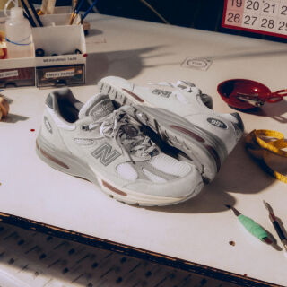 A pair of New Balance Made in UK sneakers on a white workbench surrounded by shoemaking tools and other textile equipment. 