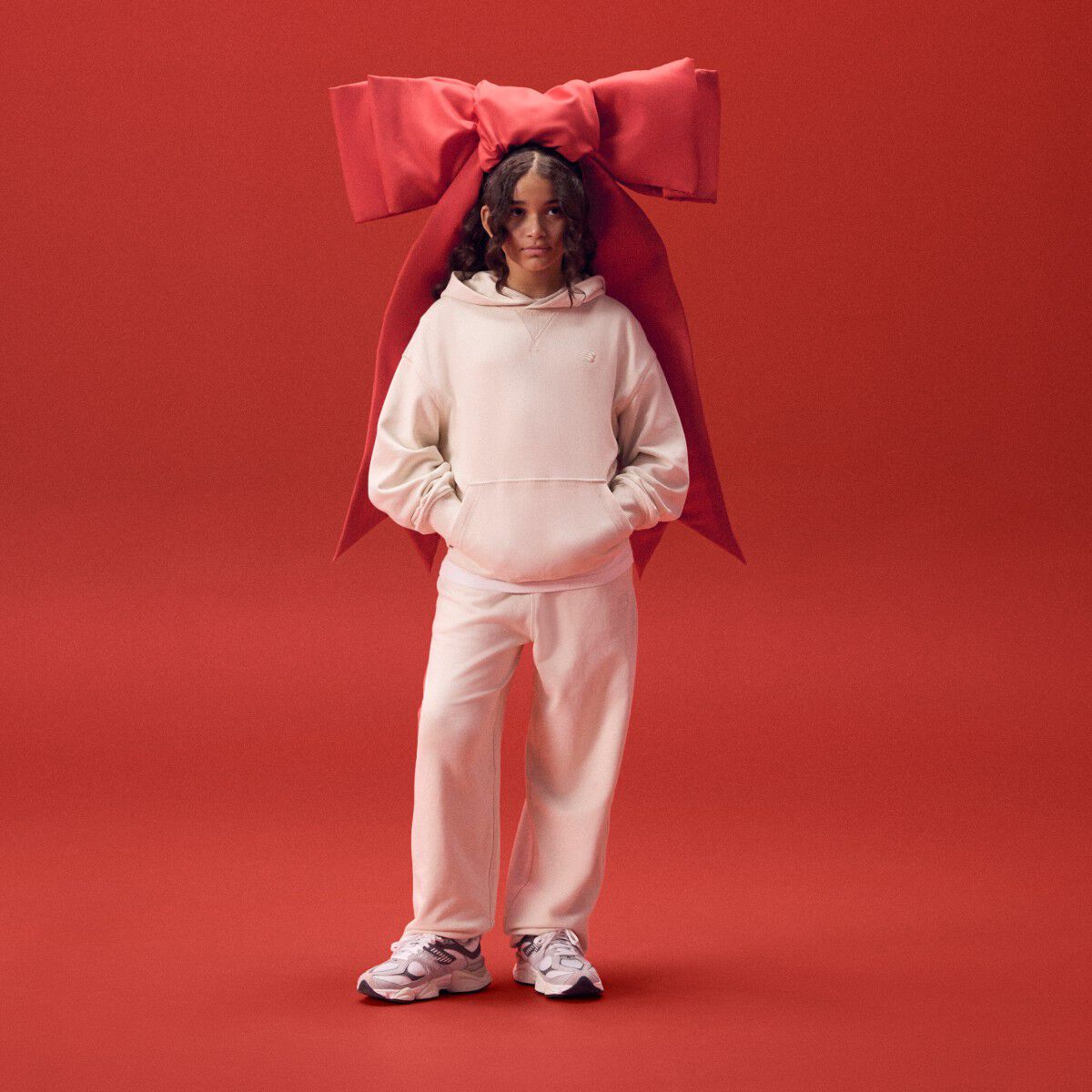 Female wearing a white matching set with a red ribbon on her head.