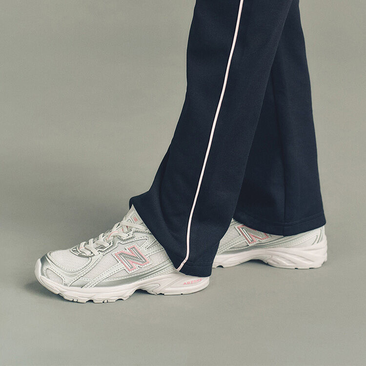 Close-up studio image of the lower legs of someone wearing New Balance sneakers against a plain light gray background.