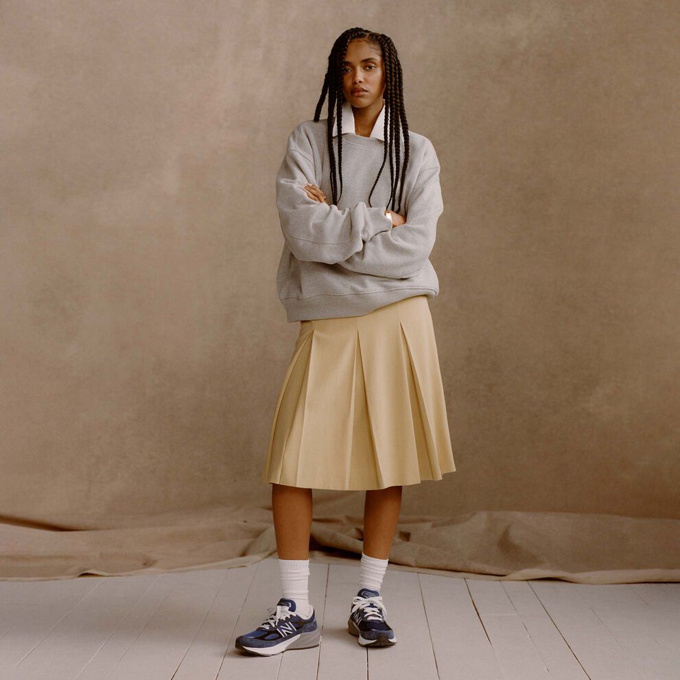 A  woman wearing blue Made in USA 990v6 shoes in front of a tan studio backdrop.