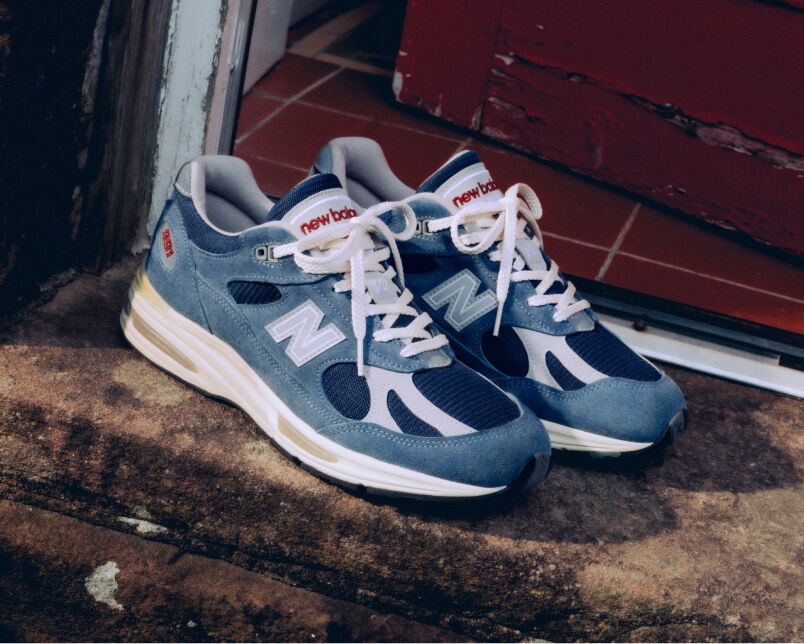 A pair of New Balance Made in UK sneakers on a white workbench surrounded by shoemaking tools and other textile equipment. 