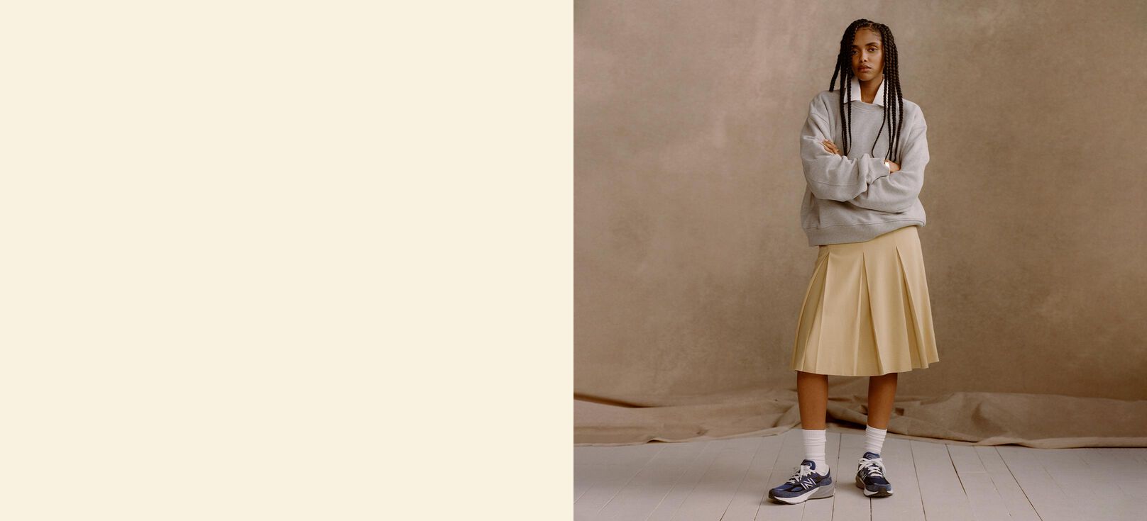 A  woman wearing blue Made in USA 990v6 shoes in front of a tan studio backdrop.